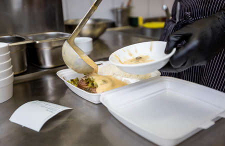 Chef preparing dish to a box in the restaurant for food delivery service to home, online ordering