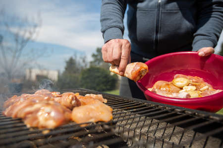 Man putting the RAW marinated chicken on a hot BBQ grill, concept of a grilling meat