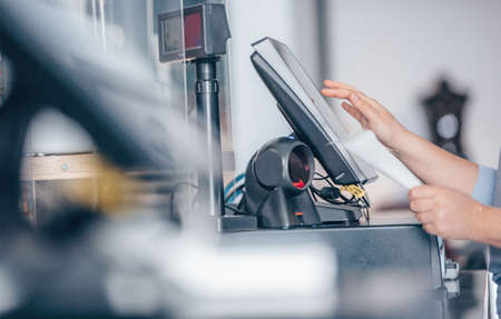 Concept of small business or sevice, woman or saleswoman in apron at counter with a cashbox working at clothes shop, touchscreen POSの写真素材