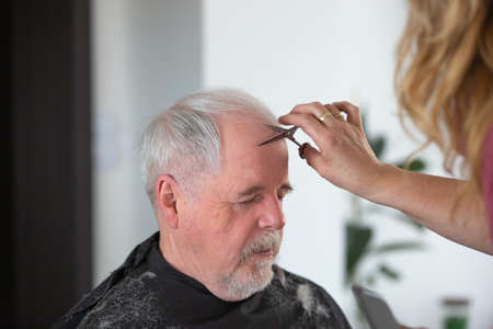 Home hairdressing concept, senior man the hair cutting by woman hairdresser