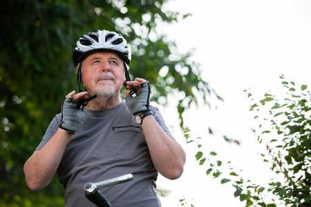 Smiling active senior man cycling or biking outside, puts on his protective helmet before his cycling in the forest, healthy lifestyle sport conceptの写真素材