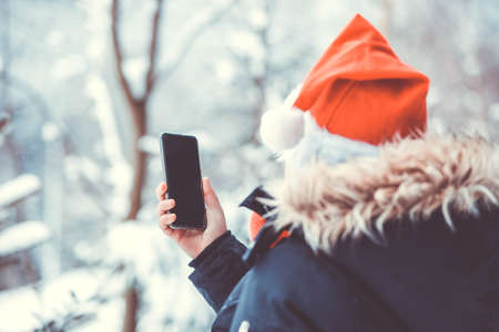 Young woman with santa hat and with a smartphone in the snowy nature, winter conceptの写真素材