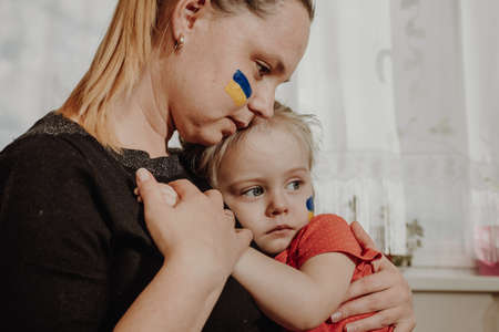 Ukrainian young mother with daughter with flag on the face with fear suffering and praying peace during war conflict between Russia and Ukraine, invasion of Russia in Ukraineの写真素材