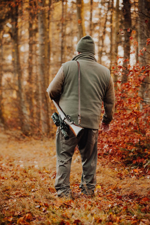 Portrait of hunter or ranger with gun or rifle in the forest looking out or hunting of some venison,...