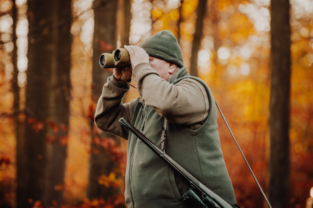Hunter or ranger with telescope looking out for wild animals in the forest, hunting period, autumn season, hunting and people conceptの写真素材