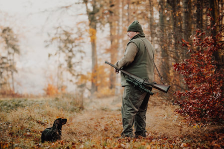 Autumn hunting season, hunter with rifle and dog looking out for some wild animal in a wood or forest, outdoor sports conceptの写真素材