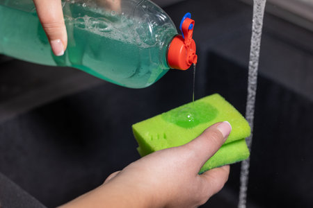 Woman uses dishwashing detergent for wash up dishes in the kitchen at homeの写真素材