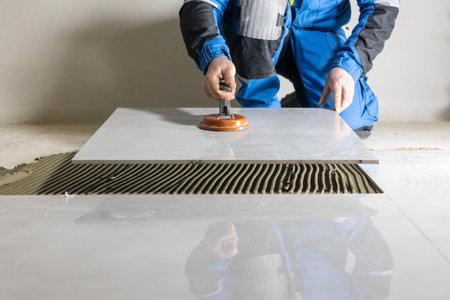 Tiler worker placing or tiling gray ceramic tile in the position over adhesive glue with lash tile...