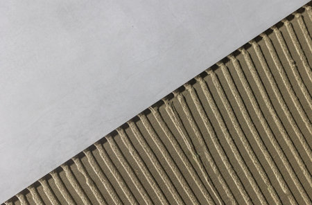 Tiler worker placing or tiling gray ceramic tile in the position over adhesive glue with lash tile leveling system, renovation or recontruction, concept of buildingの写真素材