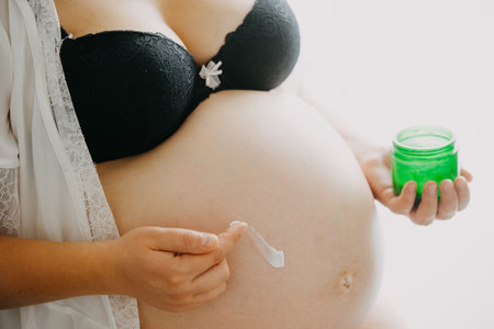 Young pregnant woman with the belly smearing cream against stretch marks, pregnancy conceptの写真素材