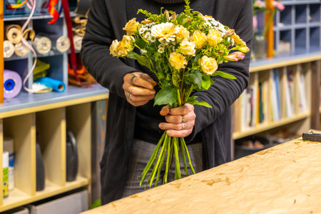 Florist arranging yellow roses and other flowers in a bouquetの写真素材
