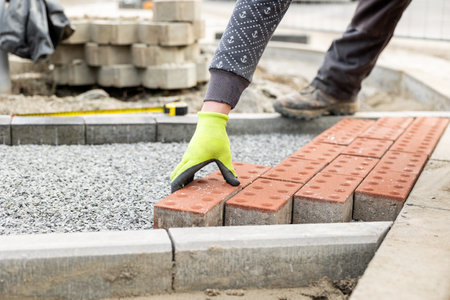 Construction worker placing red concrete paving stones in gravel bed during sidewalk constructionの写真素材