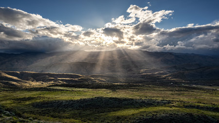 Sun Rays Piercing Clouds Over Green Fieldの写真素材