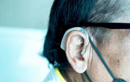 An old man wears a hearing aid, closeup