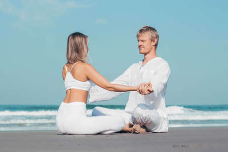 guy and girl in white clothes are sitting on the ocean and holding handsの写真素材