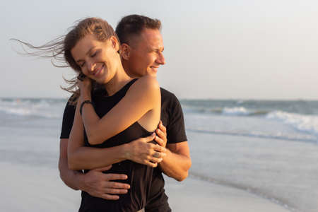 Happy couple of young men and women running, laughing and holding hands on a deserted tropical beach at sunsetの写真素材