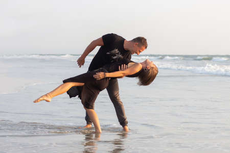 Happy couple of young men and women running, laughing and holding hands on a deserted tropical beach at sunsetの写真素材