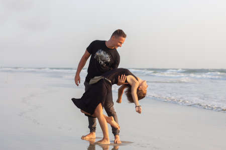 Happy couple of young men and women running, laughing and holding hands on a deserted tropical beach at sunsetの写真素材