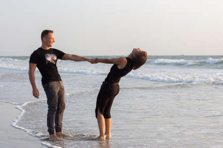 Happy couple of young men and women running, laughing and holding hands on a deserted tropical beach at sunsetの写真素材