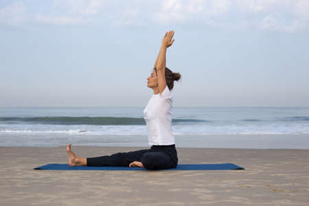 young girl on the beach doing yoga. in white clothesの写真素材