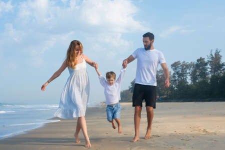 happy family dad and mom hold baby by the hands, have a rest on a tropical beachの写真素材