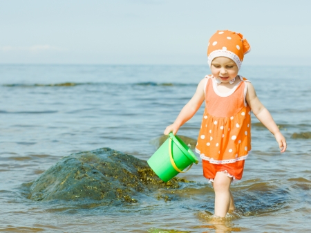 The little girl on the beach is water in the bucket.の写真素材