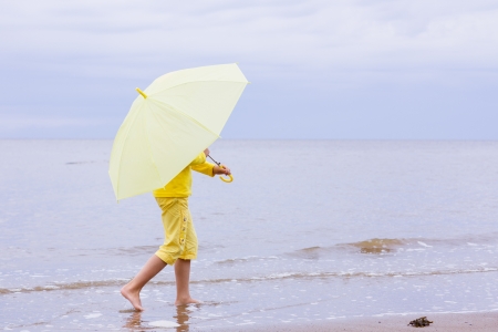The girl in yellow clothes with umbrella goes barefoot on the beach.の写真素材