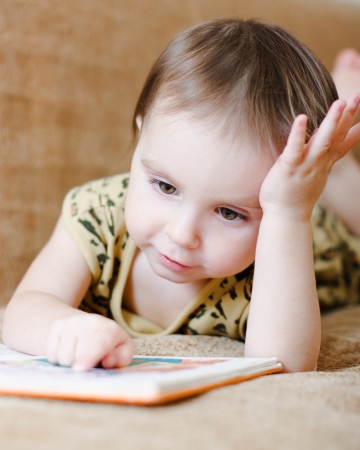 Beautiful cute baby reading a book while lying on the couch.の写真素材