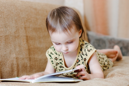 Beautiful cute baby reading a book while lying on the couch.の写真素材