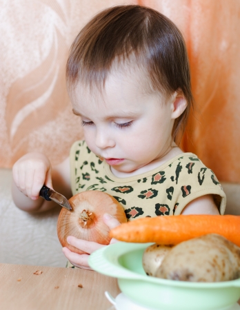 Beautiful cute kid with vegetables in the kitchen.の写真素材