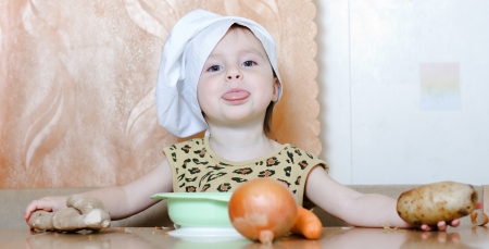Beautiful cute little cook with vegetables in the kitchen.の写真素材