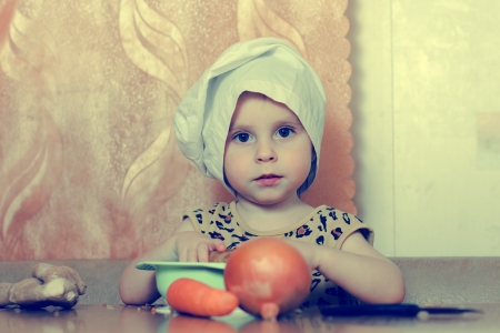 Beautiful cute little cook with vegetables in the kitchen.の写真素材