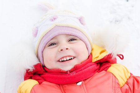 Beautiful happy kid in the red jacket in the winter outdoors.の写真素材
