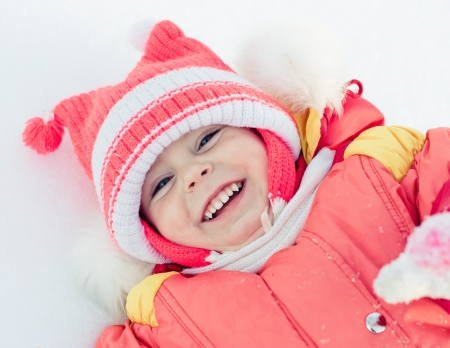 Beautiful happy kid in the red jacket in the winter outdoors.の写真素材