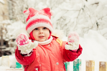 Beautiful happy kid in the red jacket in the winter outdoors shows mittens.の写真素材