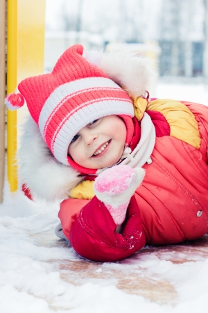 Beautiful happy kid in the red jacket in the winter outdoors.の写真素材