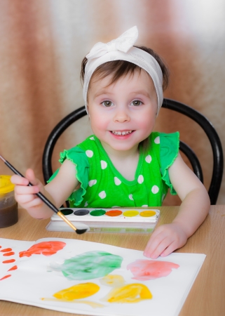 Little girl draws paints sitting at the table.の写真素材