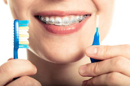 Beautiful smiling girl with retainer for teeth brushing teeth on a white background.の写真素材