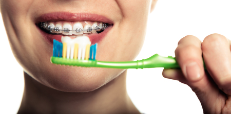 Beautiful smiling girl with retainer for teeth brushing teeth on a white background.