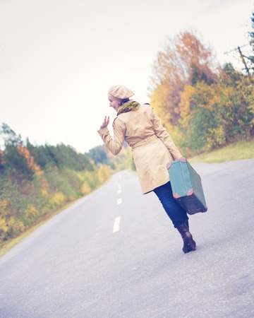 Elegant woman with a suitcase traveling the highway autumn day.の写真素材