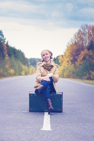 Elegant woman with a suitcase traveling the highway autumn day.の写真素材