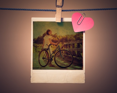 Blank instant photo girl on a bicycle and small red paper heart hanging on the clothesline. Photos in retro style.の写真素材
