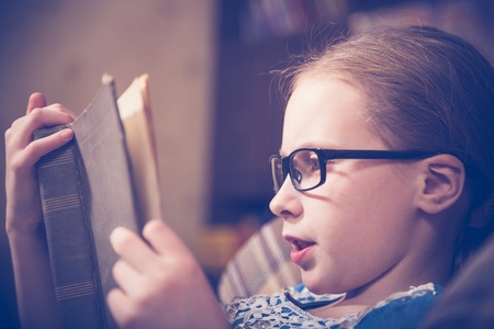 Girl reading a book at home sitting in an armchair. Photos in retro style.の写真素材