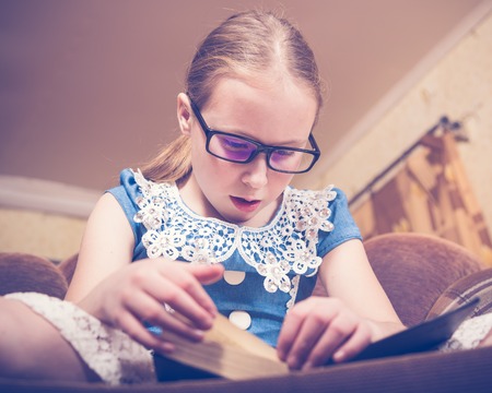 Girl reading a book at home sitting in an armchair. Photos in retro style.の写真素材