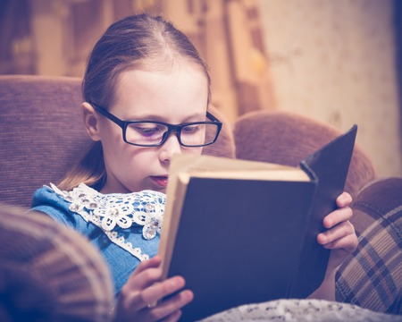 Girl reading a book at home sitting in an armchair. Photos in retro style.
