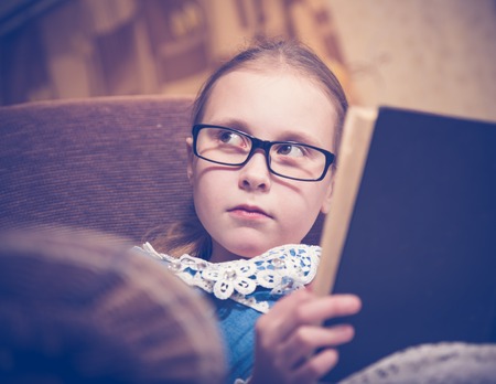Girl reading a book at home sitting in an armchair. Photos in retro style.の写真素材