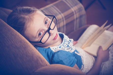Girl reading a book at home sitting in an armchair. Photos in retro style.の写真素材