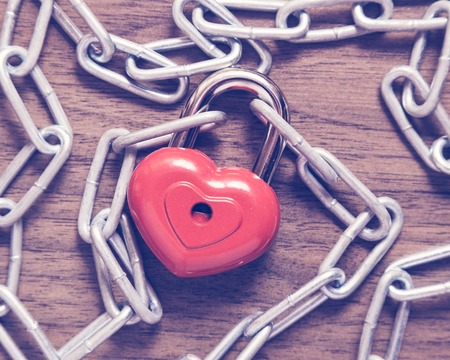 Lock heart with chain on a wooden surface.の写真素材
