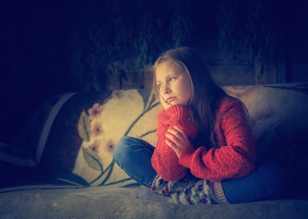 Lone teenager in warm clothing sitting on a sofa.の写真素材