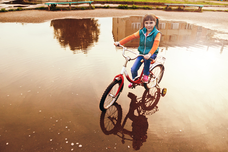 Young girl is cycling rides through a puddle in the park.の写真素材
